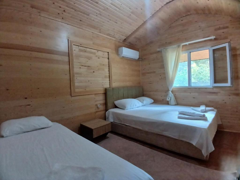 two beds in a wooden room with a window at Kalinka pansiyon in Cıralı