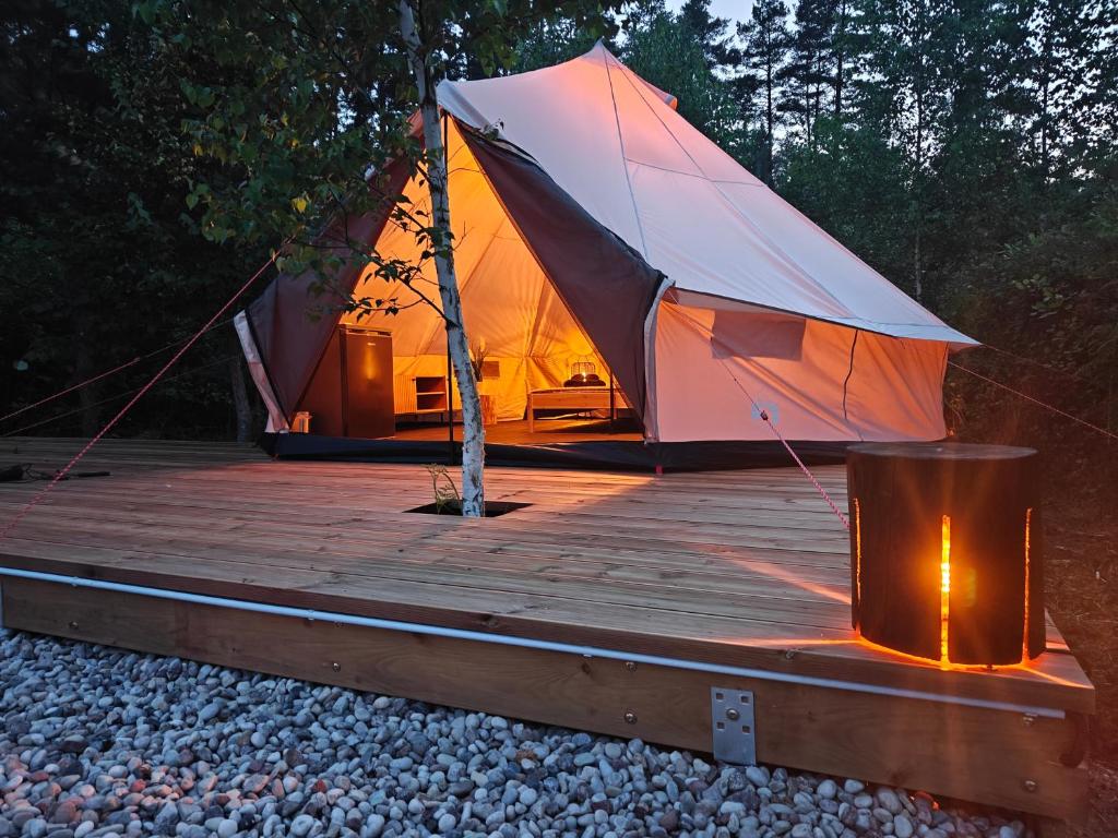 a tent with a wooden deck with a tree on it at AVOTUPJI GLEMPING telts in Allaži