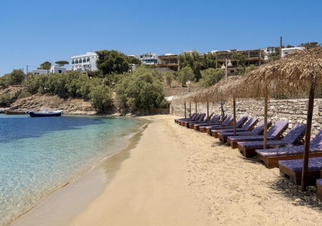 a row of beach chairs and straw umbrellas on a beach at Anchorage Paros Boutique & Private Beach in Piso Livadi