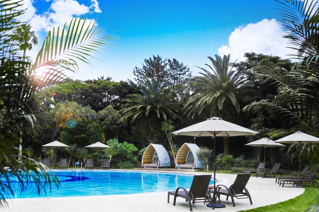a swimming pool with chairs and umbrellas and palm trees at Hotel New Otani Makuhari in Chiba