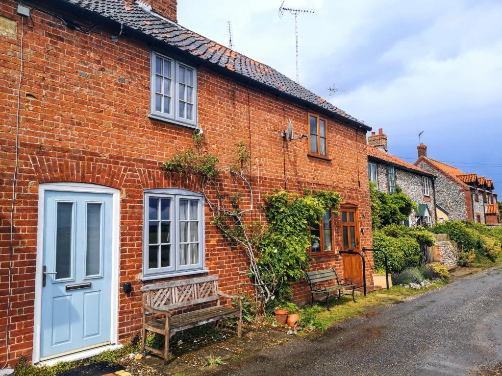 a brick house with a blue door and a bench at Priory Cottage Castle Acre in Castle Acre