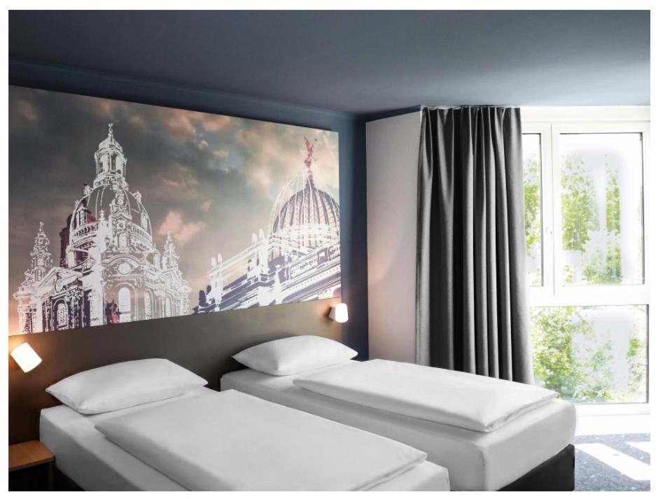 two beds in a room with a picture of a building at B&B HOTEL Dresden City-Süd in Dresden