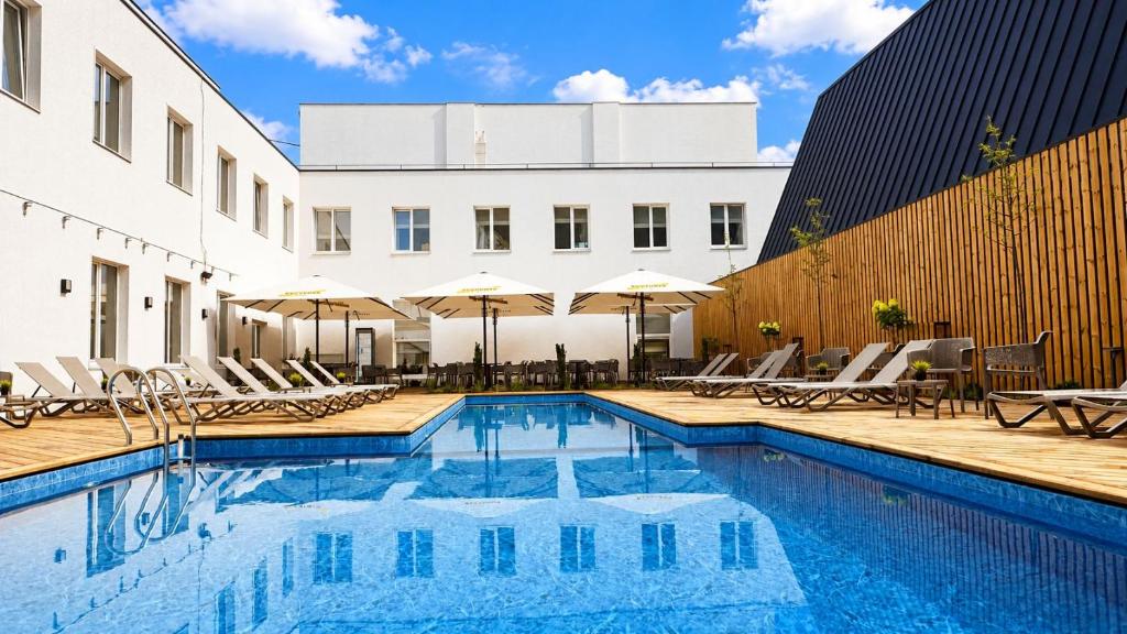 a pool with chairs and umbrellas next to a building at Nykščio Namai & SPA in Anykščiai