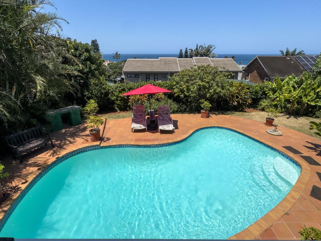 a swimming pool with two chairs and a red umbrella at Blue Nautica Coastal Retreat in Ballito