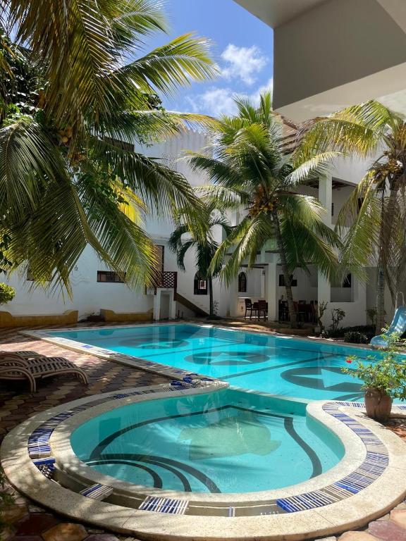 a large swimming pool with palm trees in front of a building at Jannataan Hotel in Lamu