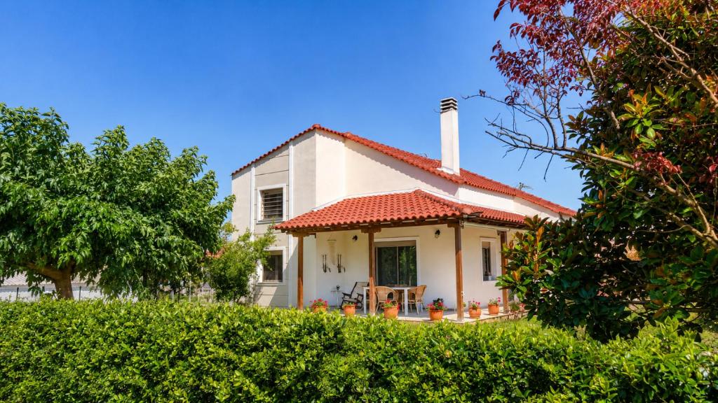 a white house with a red roof and a tree at Isidoros House in Keramoti
