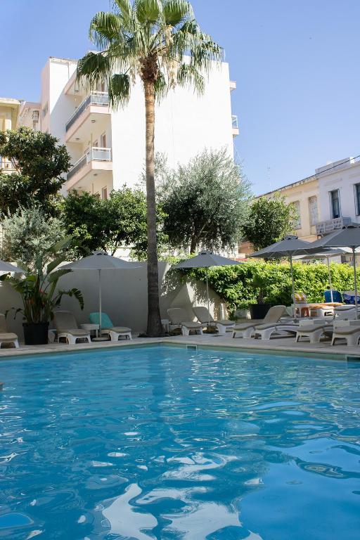 a swimming pool with chairs and a palm tree at Jason Hotel Apartments in Rethymno