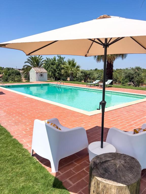 a pool with two chairs and an umbrella at Palmeira Nature Lodge in Tavira