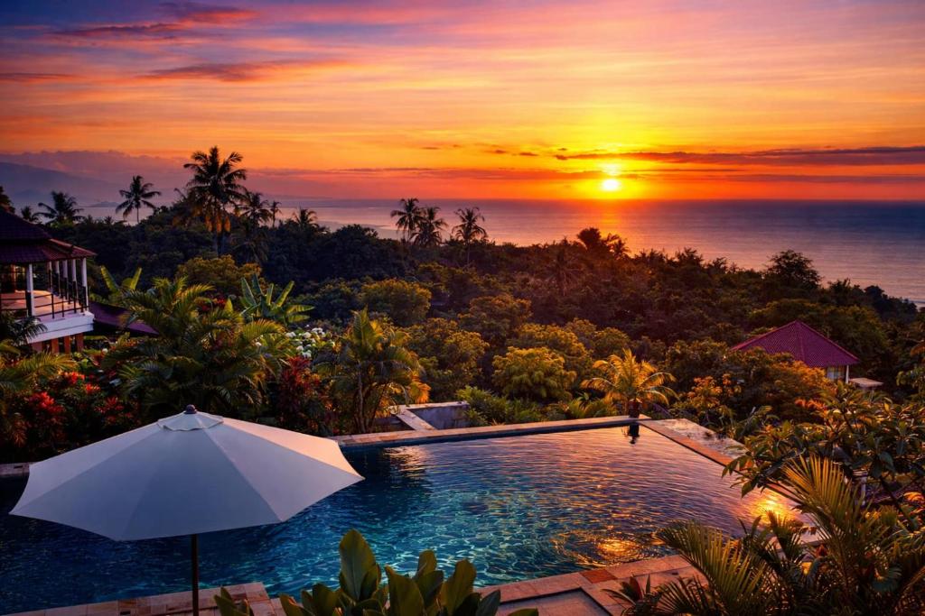 ein Pool mit Sonnenschirm vor einem Sonnenuntergang in der Unterkunft The Hamsa Bali Resort in Lovina