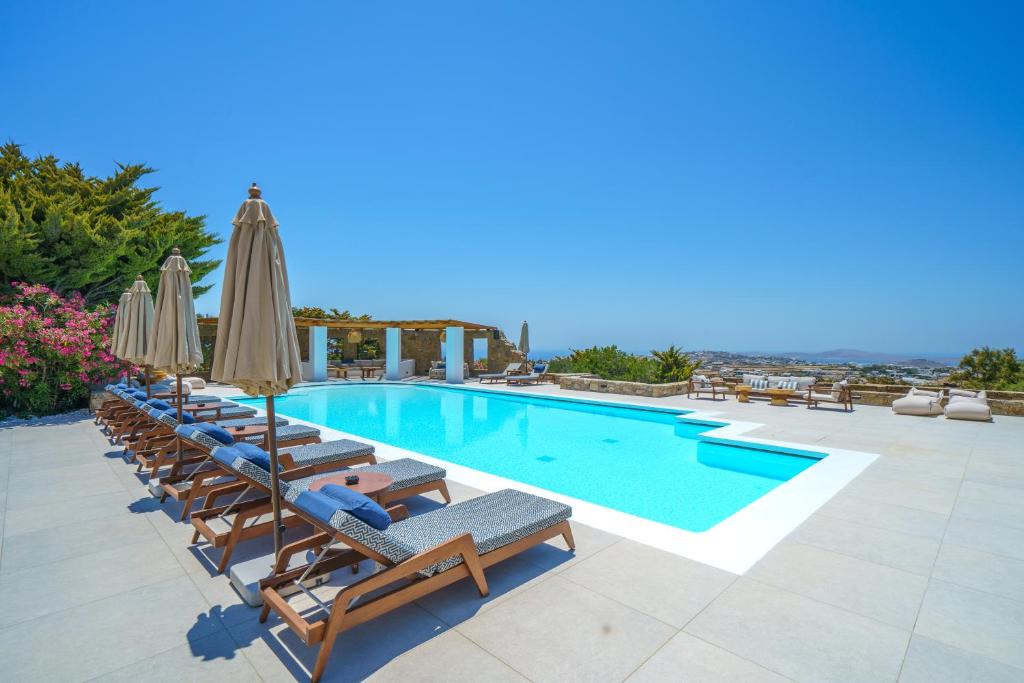 a swimming pool with lounge chairs and umbrellas at Primadonna Luxury Villas in Mikonos