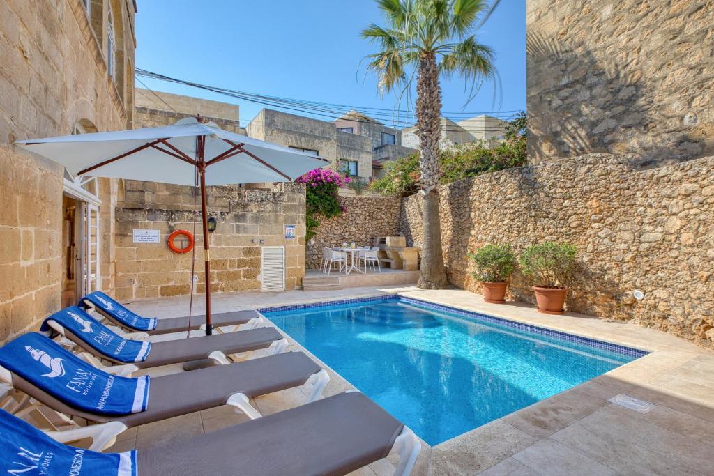 a swimming pool with lounge chairs and an umbrella at Kikka Holiday Home in Xagħra