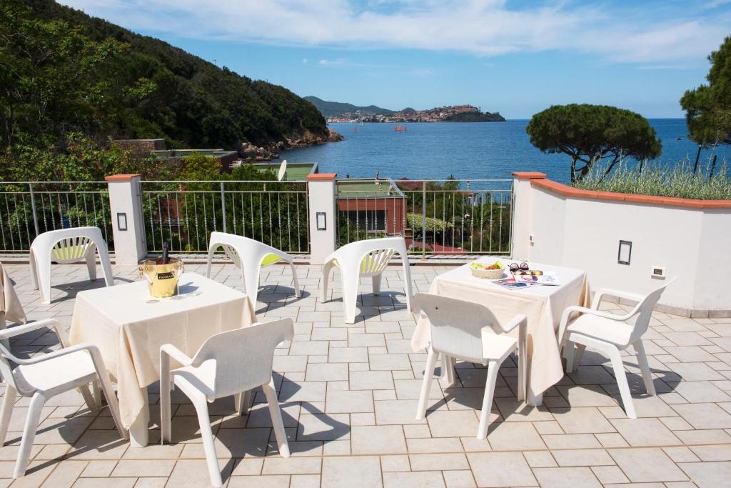 een terras met tafels en stoelen en uitzicht op het water bij Hotel Punta Pina in Portoferraio