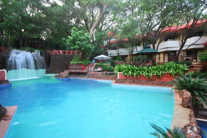 a large swimming pool with a waterfall in a yard at Horseland Hotel & Mountain Spa in Matheran