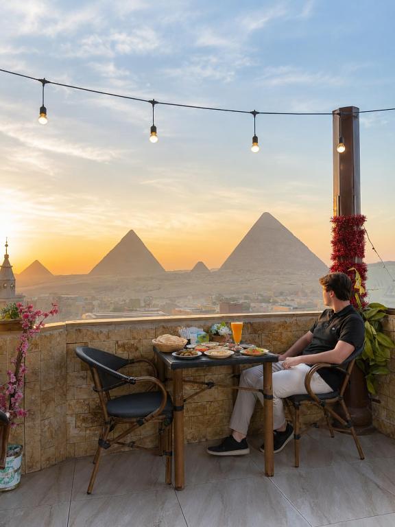 a man sitting at a table with a view of the pyramids at ImhOtep pYramids HOtel in Cairo