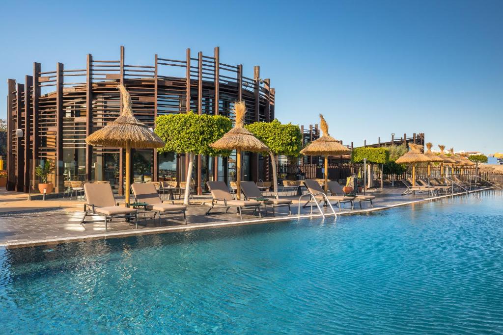 a swimming pool with chairs and umbrellas and a building at Barceló Tenerife Royal Level in San Miguel de Abona