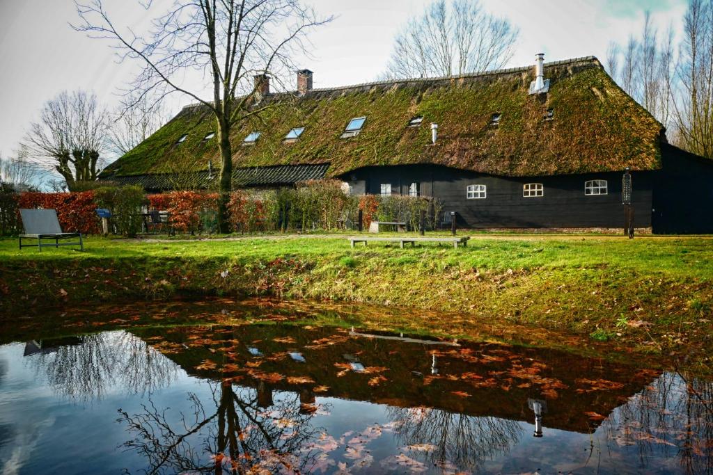 an old barn with a grass roof reflected in the water at Hof van Vijfeijken in Boxtel