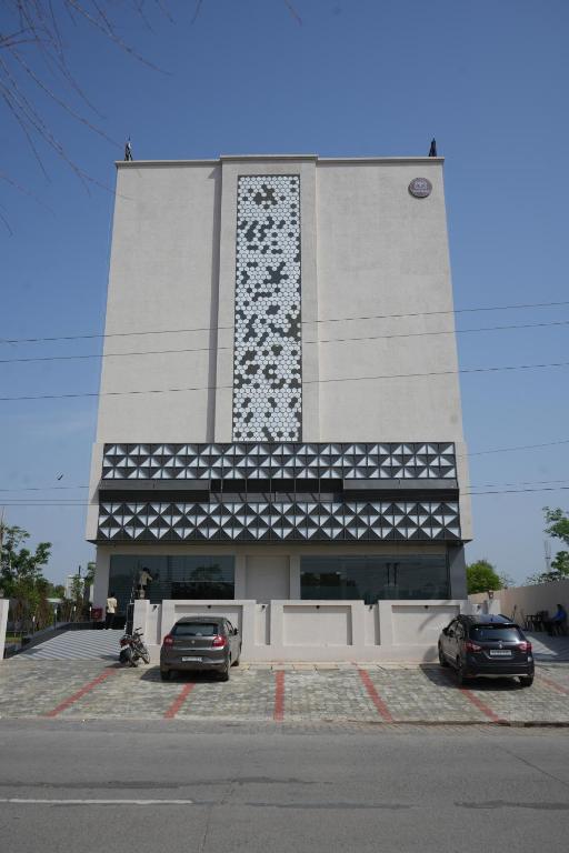 two cars parked in front of a large building at Hotel Tavijay in Jhunjhunūn