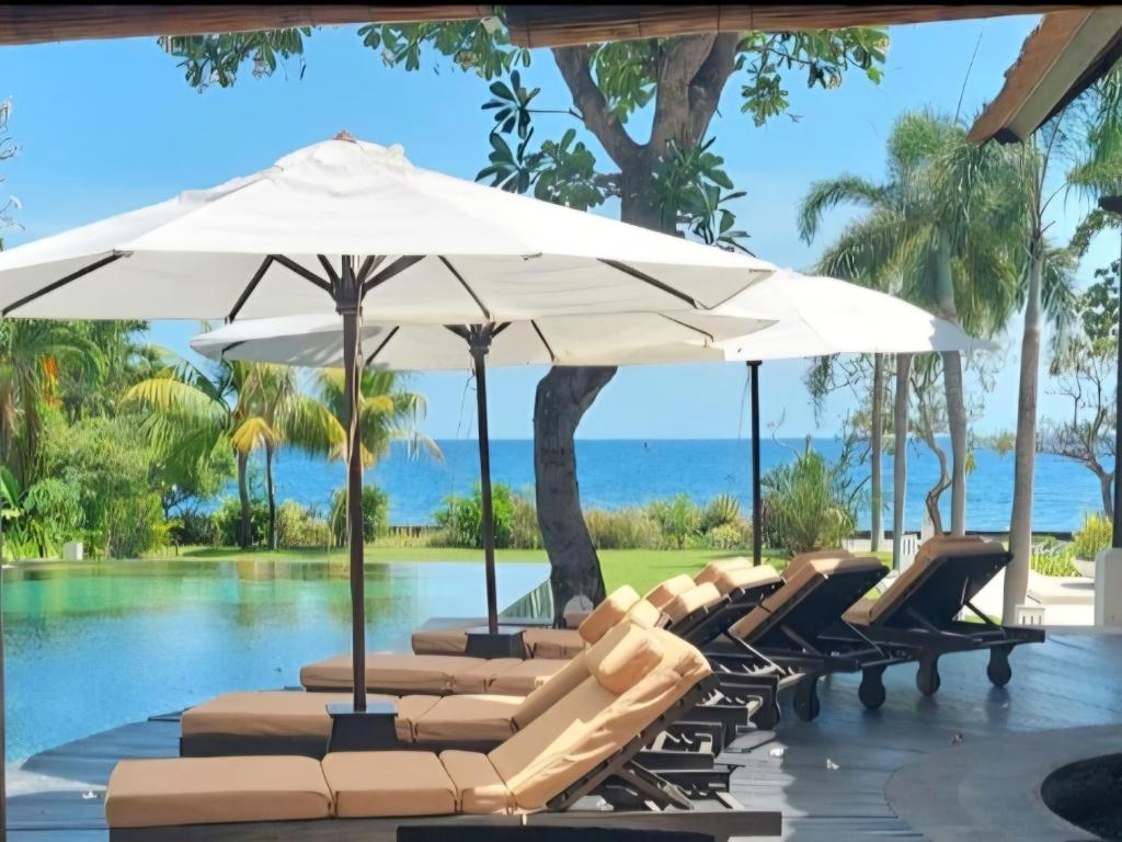 a group of lounge chairs and umbrellas next to a swimming pool at Villa Terang Bulan - luxury private beachfront villa in Pengastulan