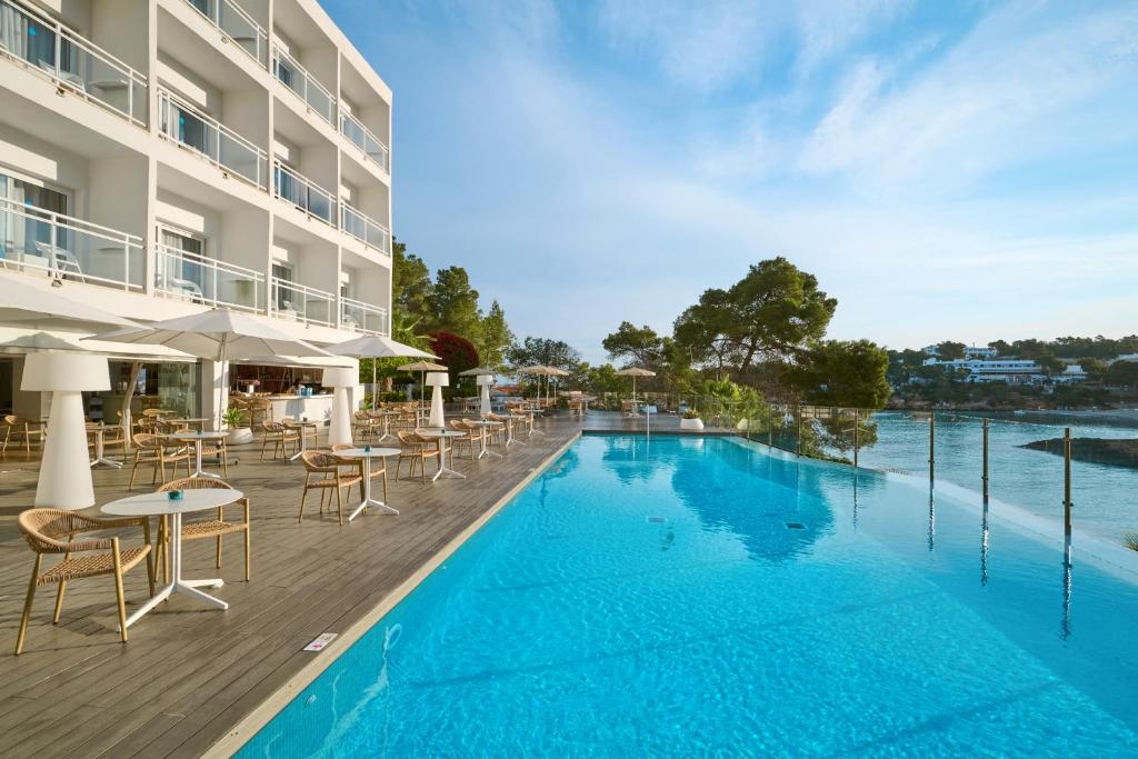 a swimming pool with tables and chairs next to a building at Grupotel Ibiza Beach Resort - Adults Only in Portinatx