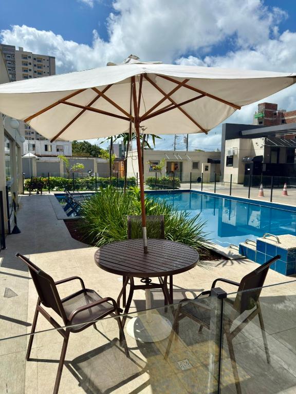 a table with an umbrella and chairs next to a pool at Auréa Residência - a 500 m da Praia in Cabedelo