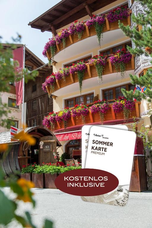 a sign in front of a building with flowers at Hotel am Dorfplatz inkl PREMIUM Sommerkarte in Sankt Anton am Arlberg