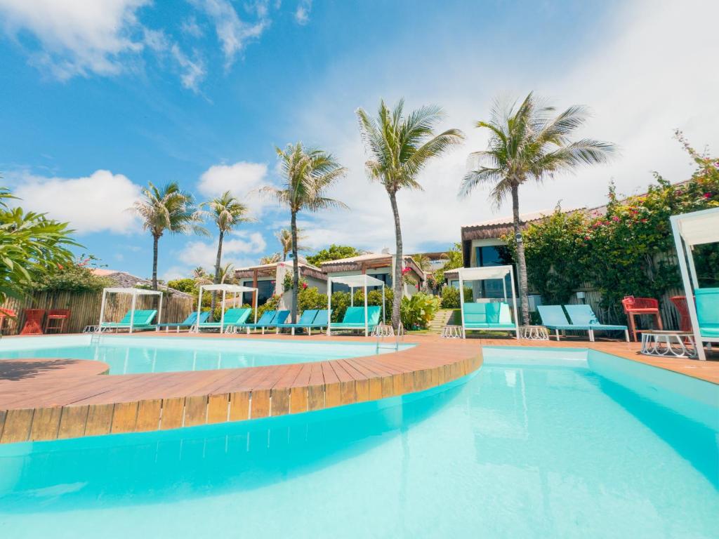 a swimming pool with chairs and palm trees at Poozendin Hotel de Charme in Canoa Quebrada