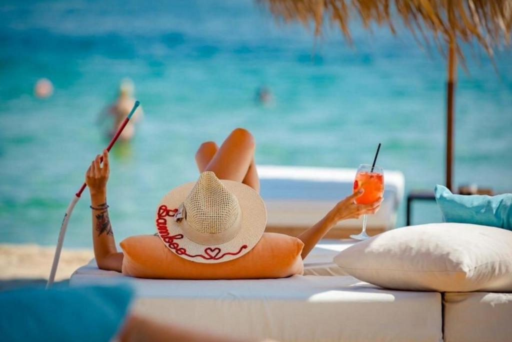 a woman in a hat sitting on a beach with a drink at Halil Bey Luxury Apartments in Kavála