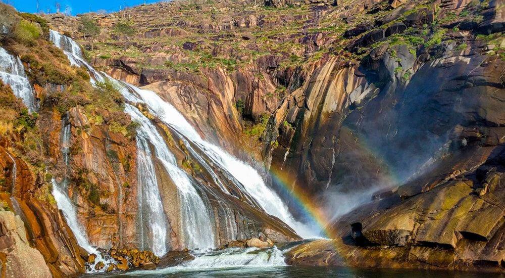 a person standing in front of a waterfall with a rainbow at Casa Ezaro in Dumbría