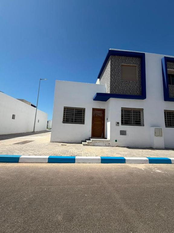 a white building with a brown door on a street at Mini Villa Azur - Bord de Mer in Driouch