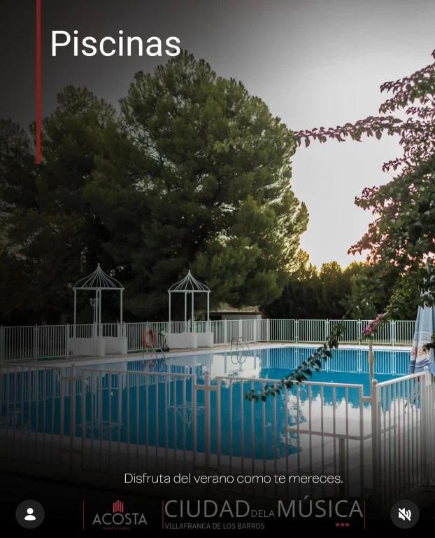 a swimming pool with a white fence and trees at Hotel Acosta Ciudad de la Música in Villafranca de los Barros