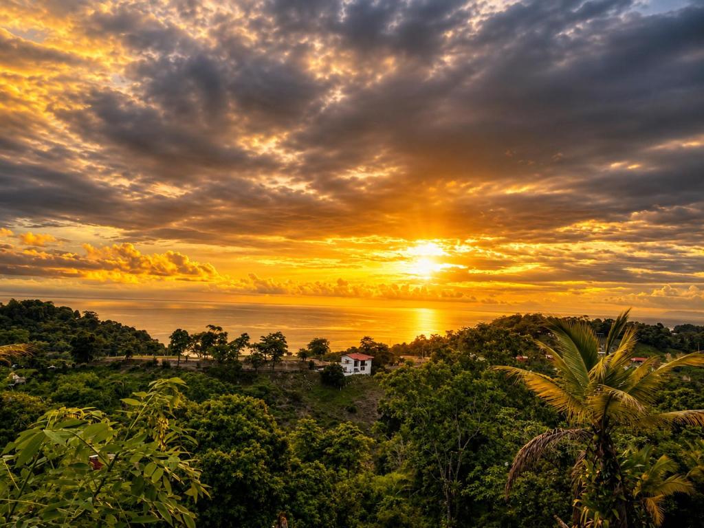 a sunset over the water with a house in the forest at Pura Natura Lodge in Manuel Antonio