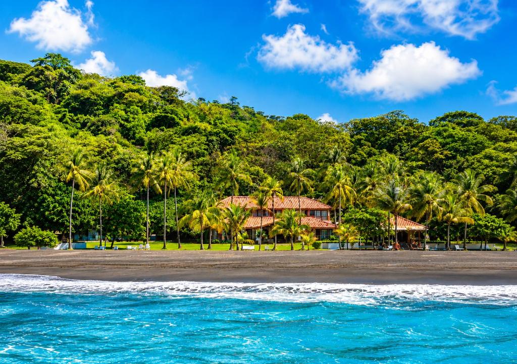 a beach with palm trees and a house at Hotel Playa Cambutal in Cambutal