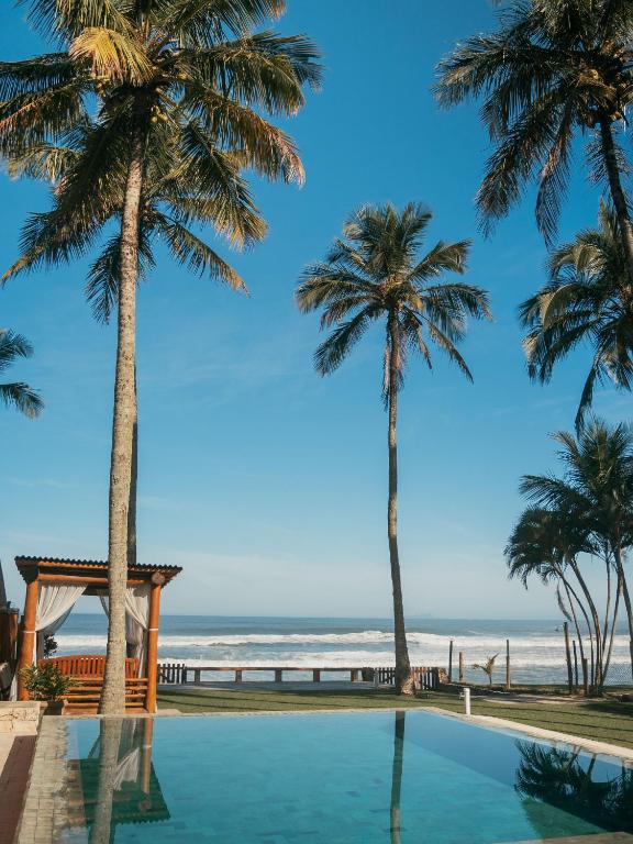 a swimming pool with palm trees and the beach at Olisa Al Mar in Maresias