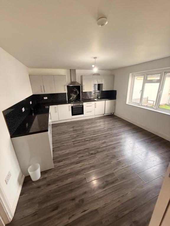 a kitchen with white cabinets and a wooden floor at 3 Bedroom Central Apartment in Goodmayes