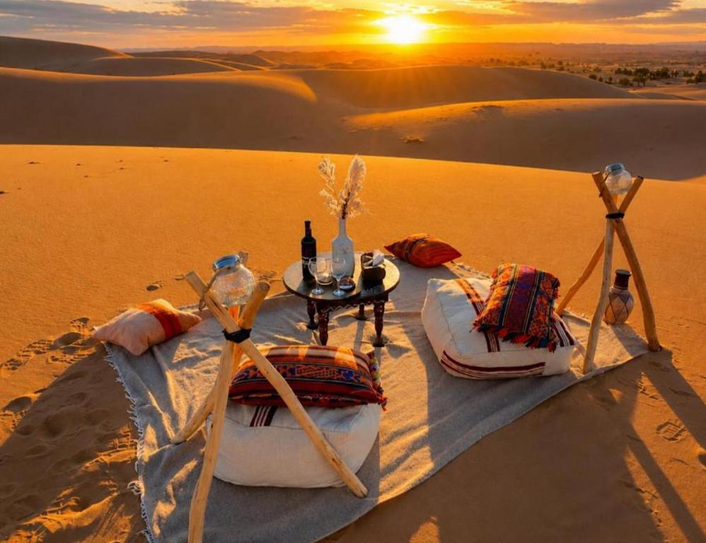a table and chairs in the desert with the sunset at Stellar Luxury Camp in Merzouga
