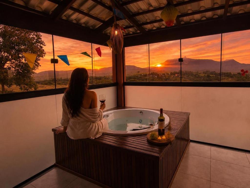 a woman sitting in a bath tub looking out the window at Chácara Sol e Lua dos três Morros in Piatã