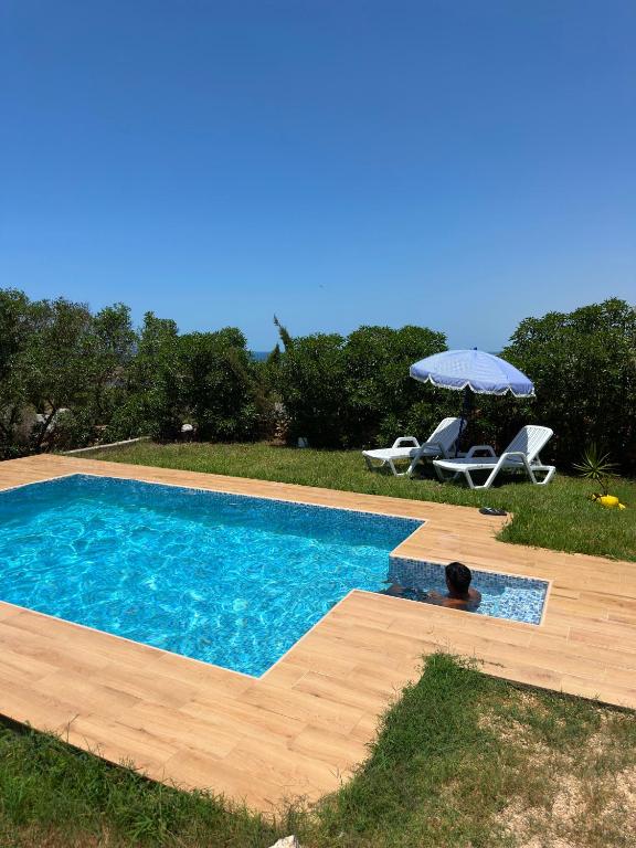 a swimming pool with an umbrella and a table and chairs at Villa Basmat in Oualidia