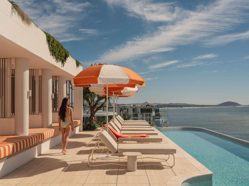 a woman walking on the balcony of a house with a pool at Avani Mooloolaba Beach Hotel in Mooloolaba