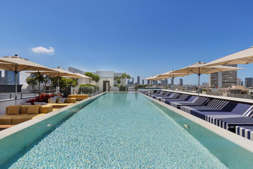 a swimming pool with chairs and umbrellas on a building at Dizengoff 99 by Isrotel Design in Tel Aviv