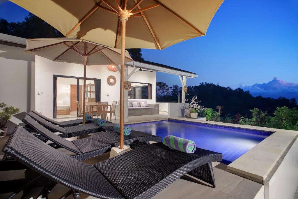a villa with a swimming pool with chairs and umbrellas at Villa Panoramic in Nusa Penida