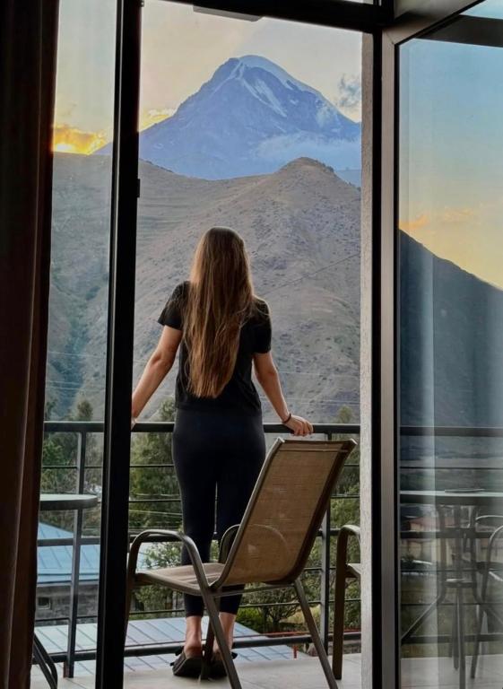 a woman standing on a balcony looking out at a mountain at 3100 Boutique Hotel Kazbegi in Kazbegi