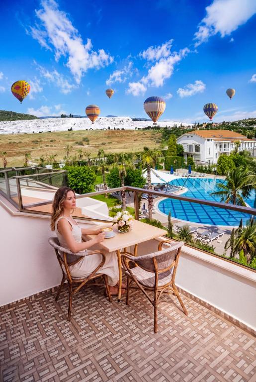 a woman sitting at a table on a balcony with hot air balloons at Tripolis Hotel in Pamukkale