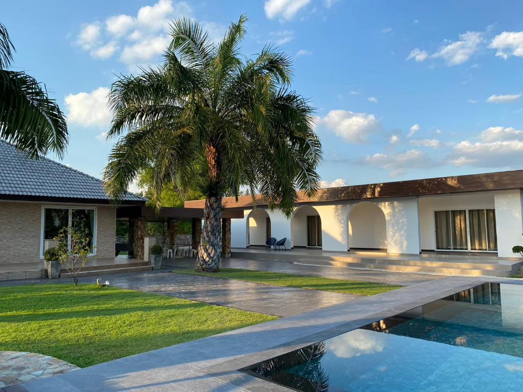 a palm tree in front of a house with a swimming pool at Arom Pool Villa Pattaya 2 in Na Jomtien