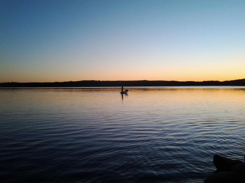 uma pessoa em um barco em um lago ao pôr do sol em Strandbo em Förby