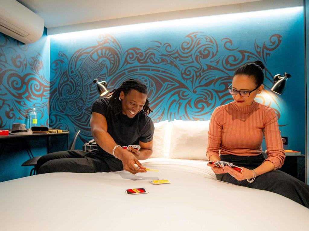 a man and woman sitting on a bed playing a game at Ibis Styles Paris Gare de l'Est Magenta in Paris
