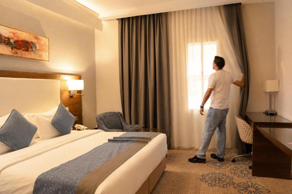 a man standing in a hotel room looking out the window at فندق فربيون المجاردة - Ferbion Hotel Almajardah in Al Majaridah