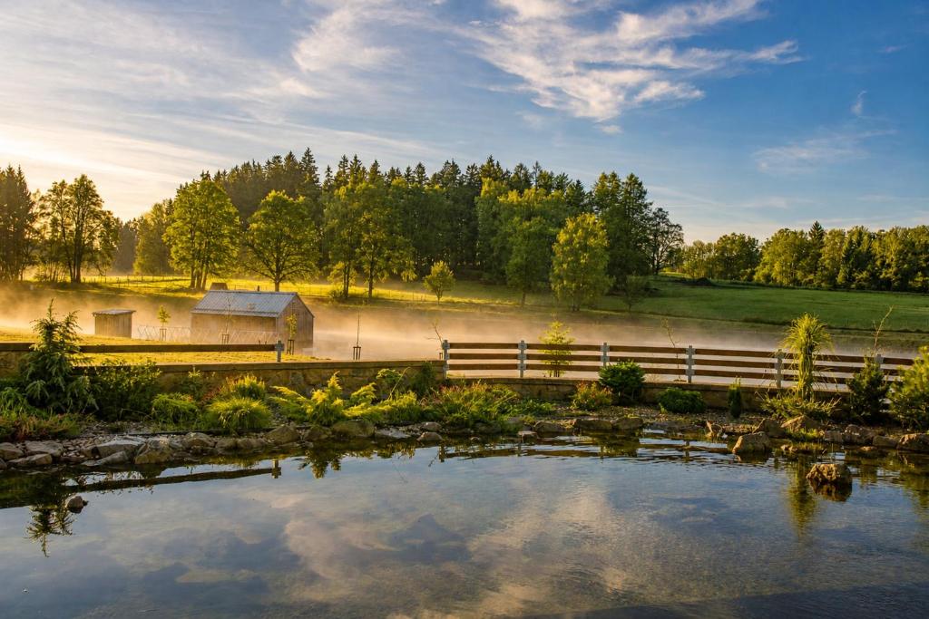a pond with a fence and a barn and trees at Amenity Usedlost v Marinkách in Blažejov