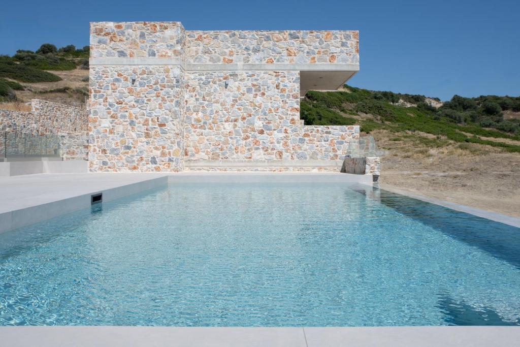 a pool with blue water next to a stone wall at Stone Luxury Suites in Agioi Apostoli