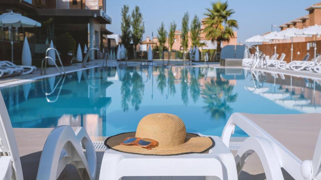 a straw hat and sunglasses sitting on a chair next to a swimming pool at Hotel Granada Palace, Affiliated by Melia in Monachil