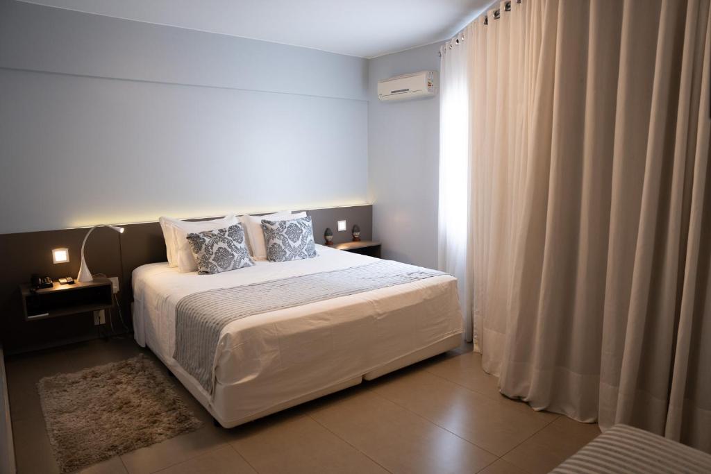 a bedroom with a bed and a window with curtains at Hz Hotel in Patos de Minas
